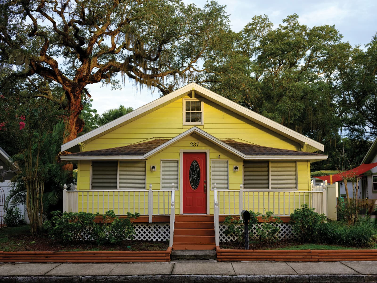 Yellow Florida bungalow home with a red front door and white porch railing